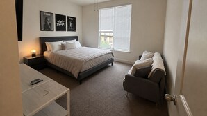 Quarto com cama, mesa de cabeceira, escrivaninha, cadeira, ventilador de teto e janela com persianas.
