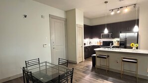 Uma cozinha moderna com área de jantar, com uma mesa e cadeiras de vidro, piso de madeira e iluminação pendente.