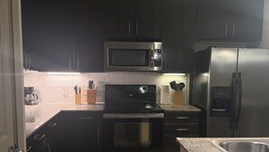 Cozinha compacta com armários escuros, geladeira de aço inoxidável, micro-ondas e forno.