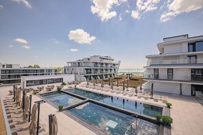 Une piscine sur le toit, agrémentée de chaises longues et de parasols, entourée de bâtiments modernes dotés de balcons.