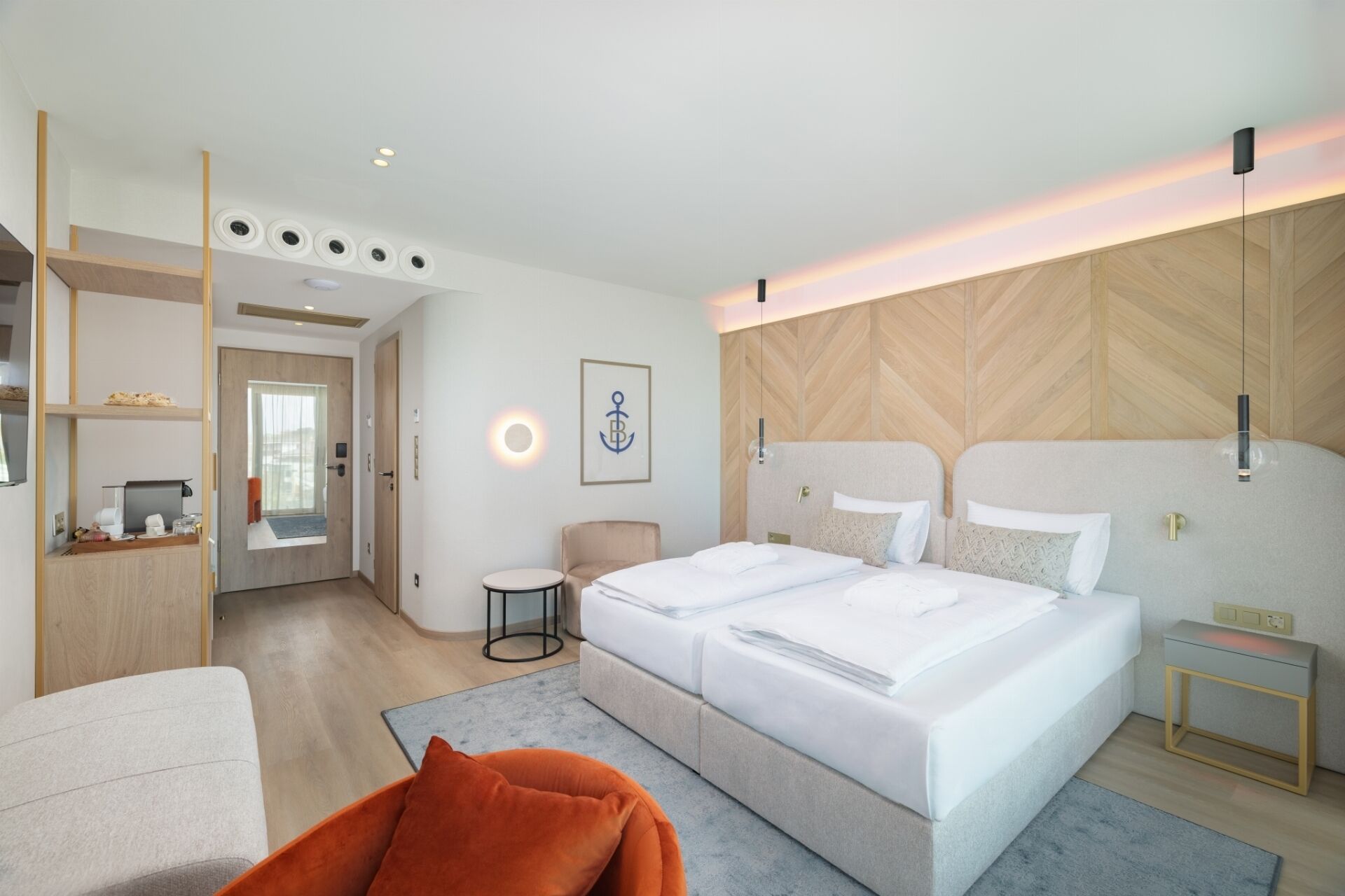 A modern hotel room with a double bed, a desk with a computer, a chair, and a small round table.