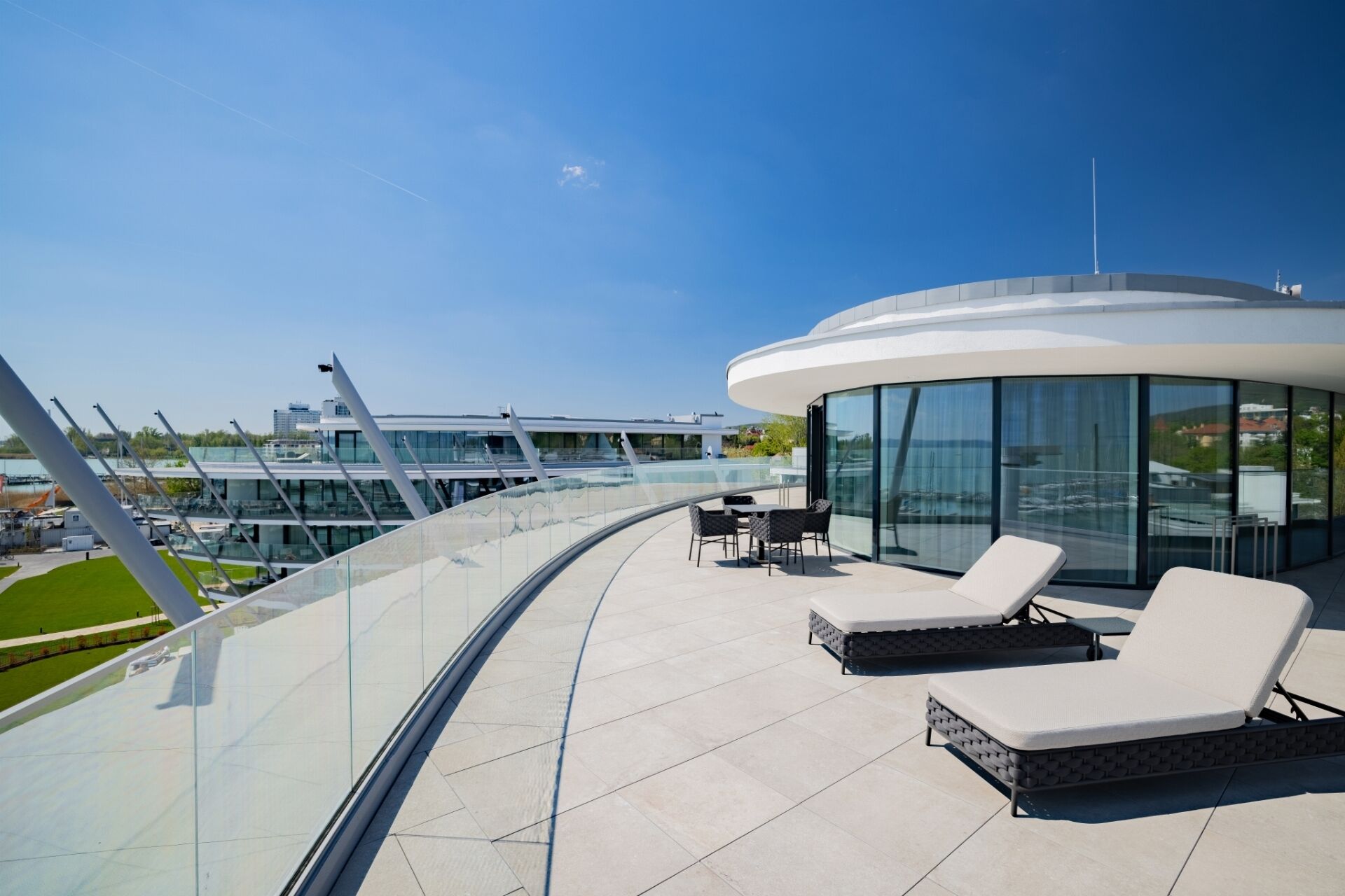 A modern outdoor lounge area with seating and a glass balustrade overlooking a marina.