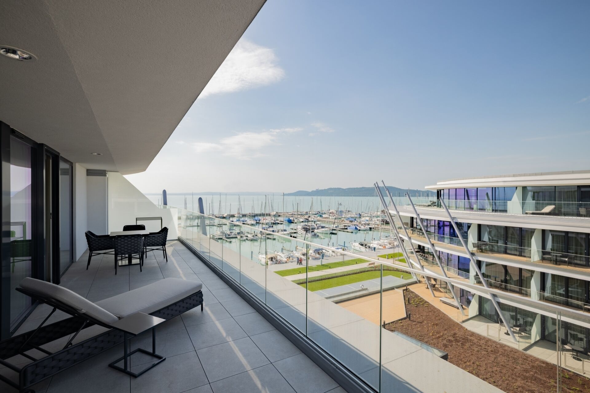 A balcony with a view of a marina, a dining area with chairs, and a modern building with glass windows.