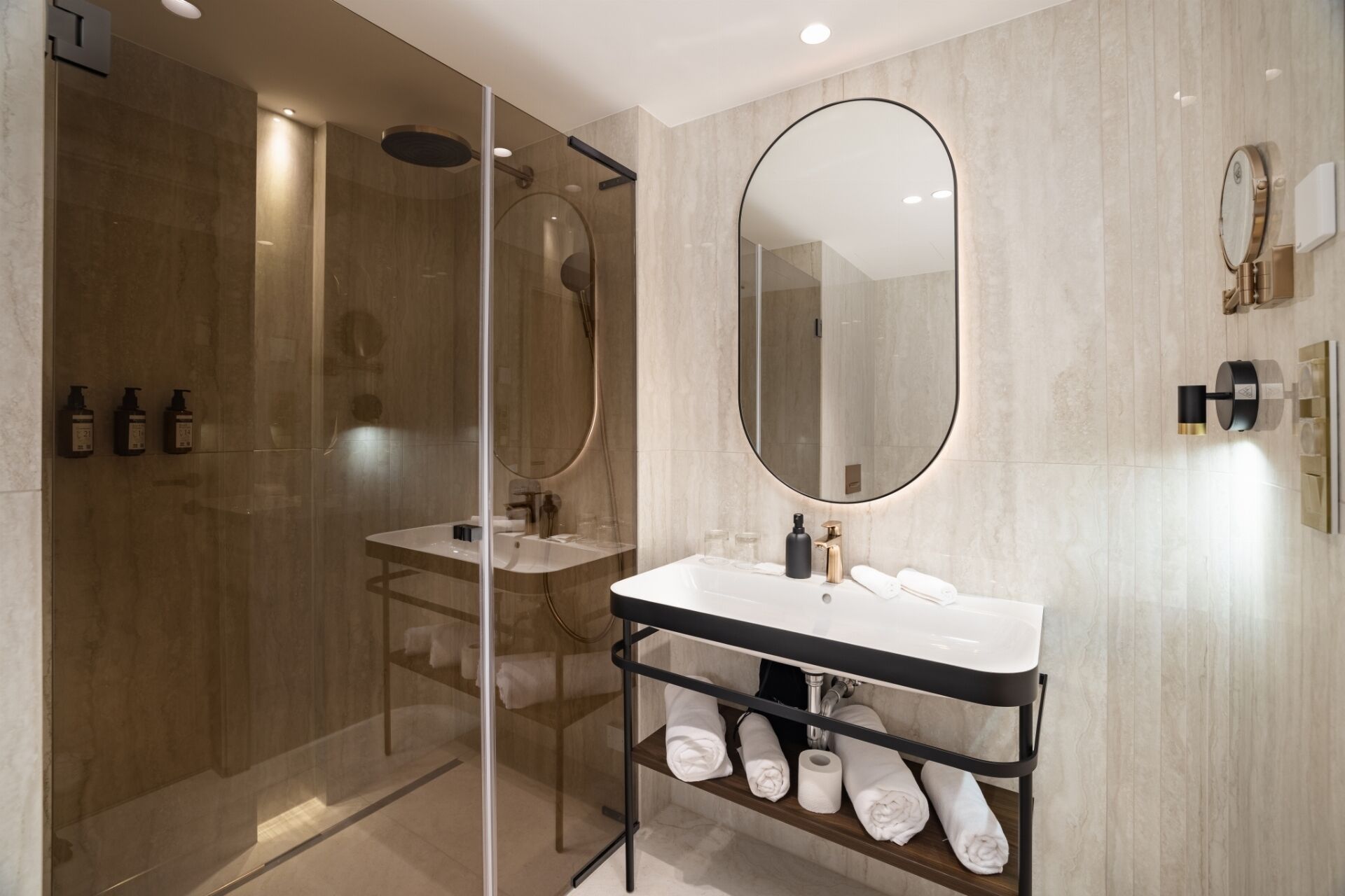 A modern bathroom with a glass-enclosed shower, a white sink with a black countertop, and a large mirror.
