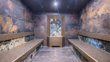 Un sauna con dos bancos, una pared central con una obra de arte texturizada y suelo de baldosas.