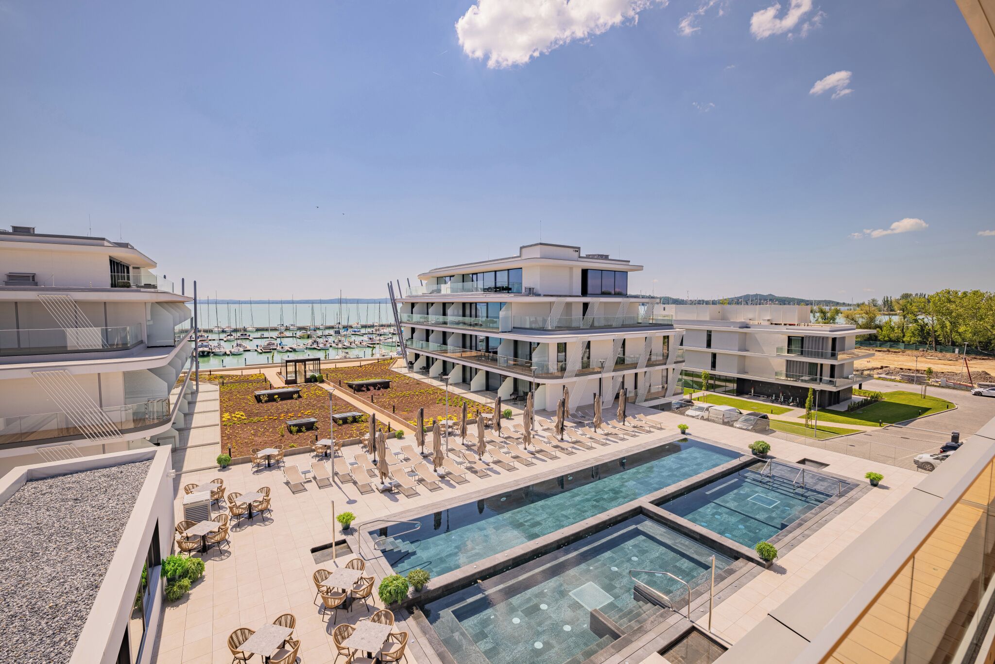 Un hotel moderno con piscina en la azotea, zona de estar al aire libre y vista al puerto deportivo.