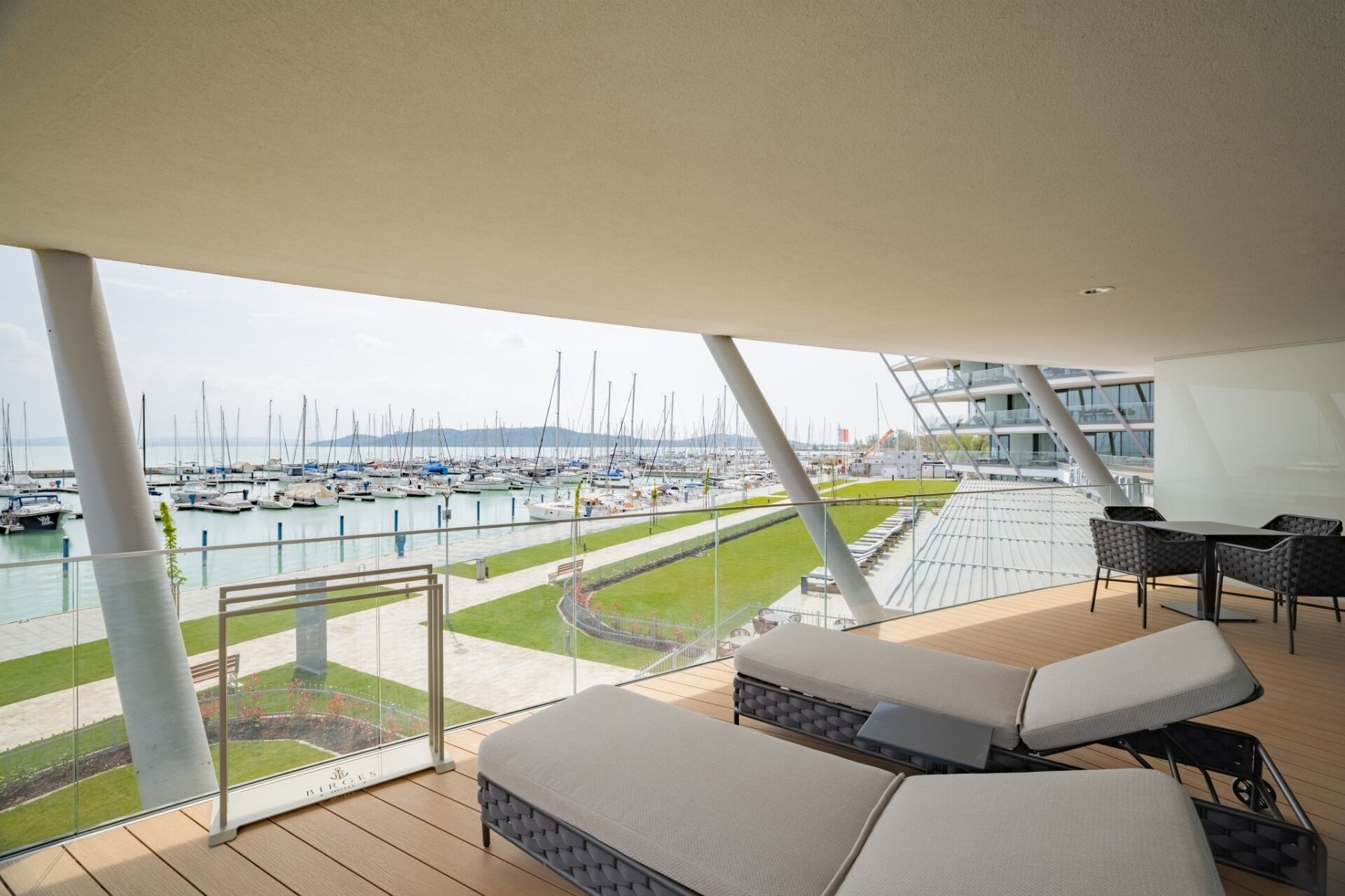Un balcón con vista a un puerto deportivo, mobiliario exterior y una estructura de edificio moderna.
