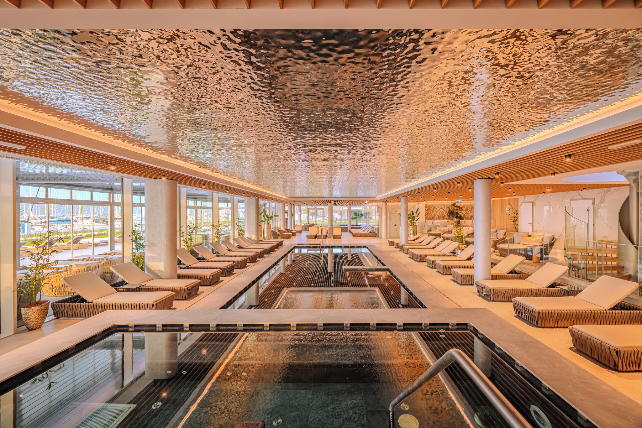 A modern spa with a central pool, lounge areas, and large windows offering views of the marina.