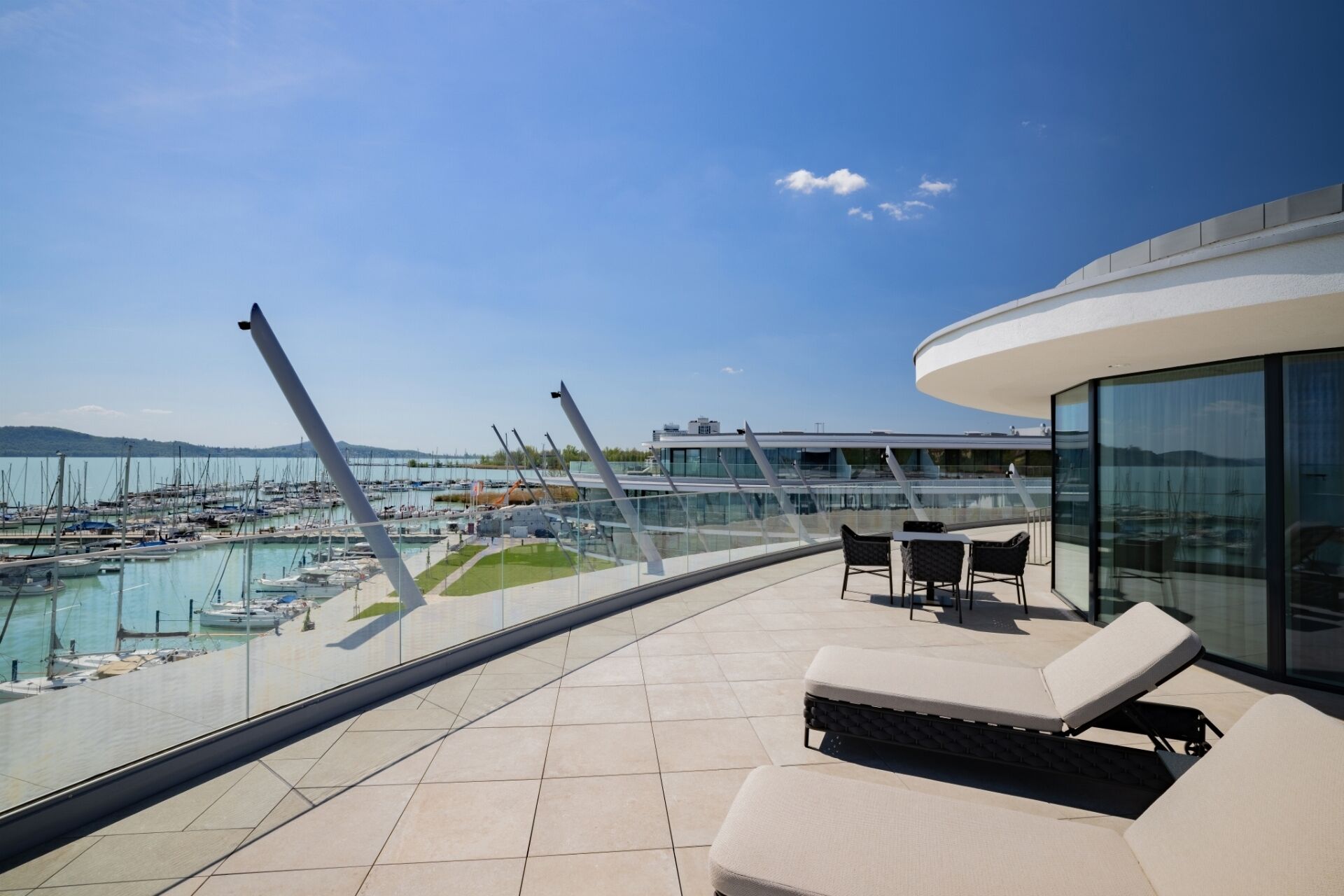 Terraza moderna en la azotea con vistas a un puerto deportivo, que cuenta con sillones de descanso y barandilla de cristal.