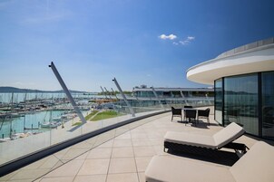 Terraza moderna en la azotea con vistas a un puerto deportivo, que cuenta con sillones de descanso y barandilla de cristal.