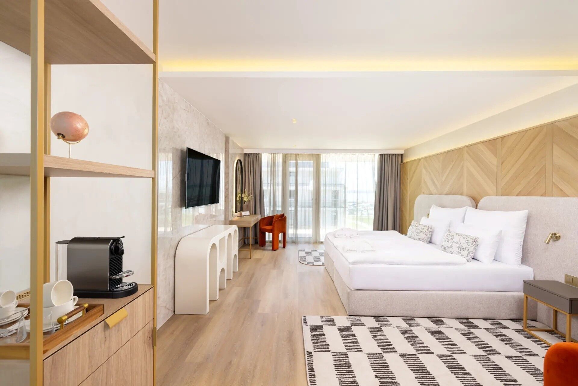 Ein modernes Hotelzimmer mit einem großen Bett, einem Flachbildfernseher, einem Schreibtisch und Blick ins Freie.
