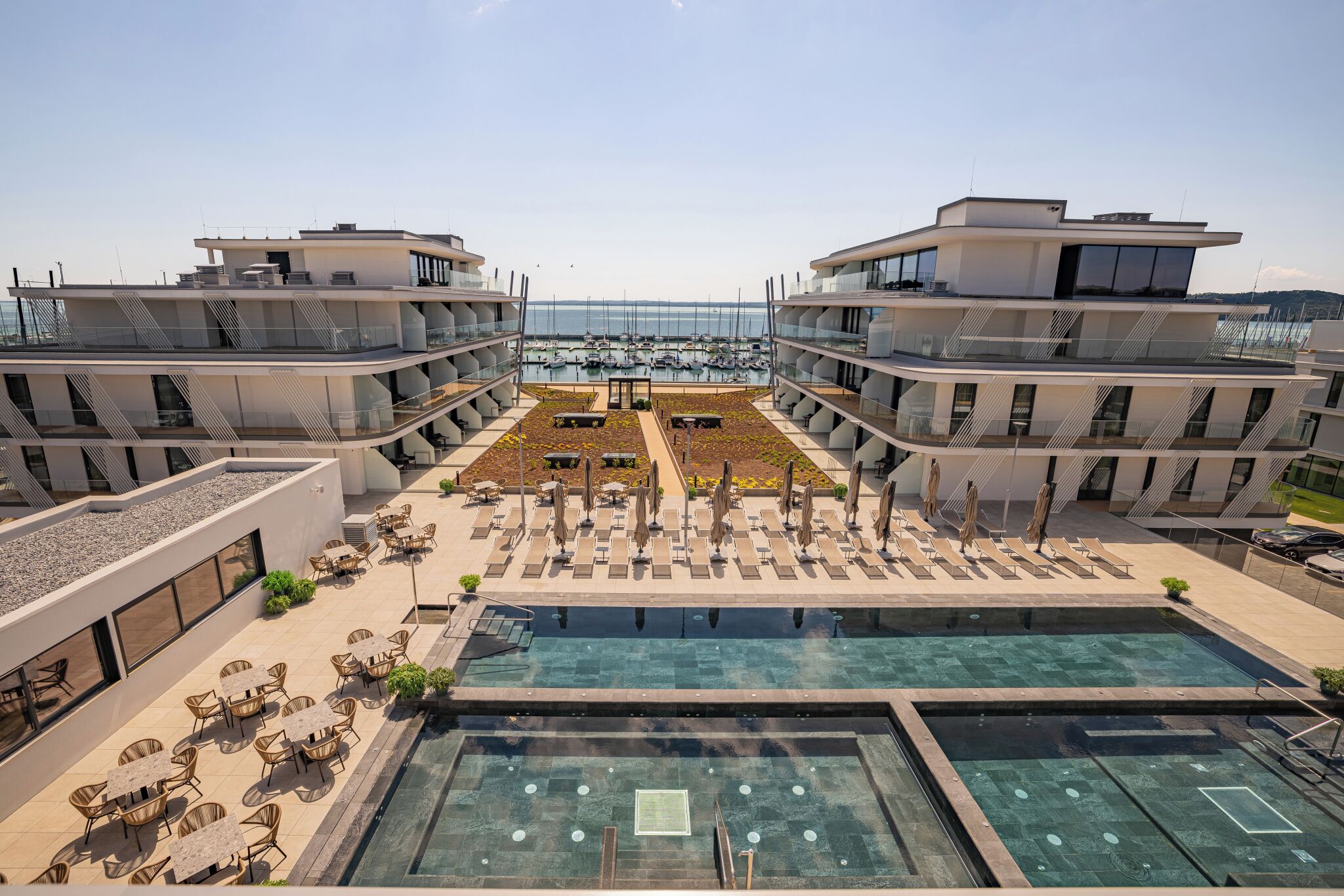 Un hotel moderno con piscina en la azotea, zona de estar al aire libre y vistas al puerto deportivo.