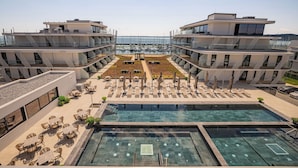 Un hotel moderno con piscina en la azotea, zona de estar al aire libre y vistas al puerto deportivo.