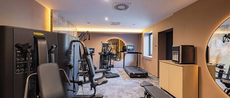 Un gimnasio con máquinas de cardio, equipo de pesas y un espejo grande.