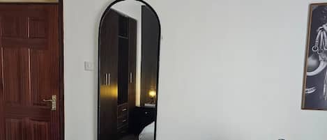 A hotel room with a bed, a mirror, a door, and a chair.