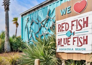A sign for Red Fish Blue Fish Pensacola Beach with a heart symbol and a fish graphic. - Gulf Front Condo at Seahorse Condos | Dog Friendly | Sleeps 9 (Pensacola Beach)