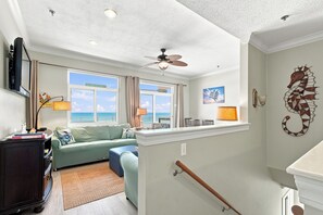 A room with a ceiling fan, a view of the ocean through large windows, a seahorse wall decoration, and a wooden bench. - Gulf Front Condo  at Seahorse Condos | Dog Friendly | Sleeps 9 (Pensacola Beach)