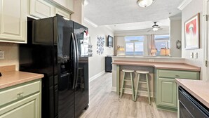 Eine Küche mit einem schwarzen Kühlschrank, grünen Schränken, einer Bar mit Barhocker und Blick aus dem Fenster.