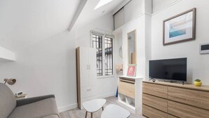 A modern living room with a sofa, a TV, a small table, and a cabinet. - Charming Studio Near the Eiffel Tower (Paris)