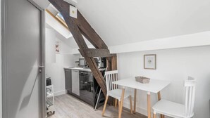 A compact kitchen with a wooden staircase, a white table with chairs, and a small refrigerator. - Charming Studio Near the Eiffel Tower (Paris)