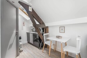 A compact kitchen with a wooden staircase, a white table with chairs, and a small refrigerator. - Charming Studio Near the Eiffel Tower (Paris)
