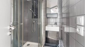 A modern bathroom with a glass-enclosed shower, a white sink, and a tiled wall. - Charming Studio Near the Eiffel Tower (Paris)