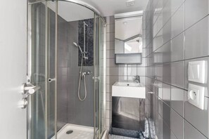 A modern bathroom with a glass-enclosed shower, a white sink, and a tiled wall. - Charming Studio Near the Eiffel Tower (Paris)