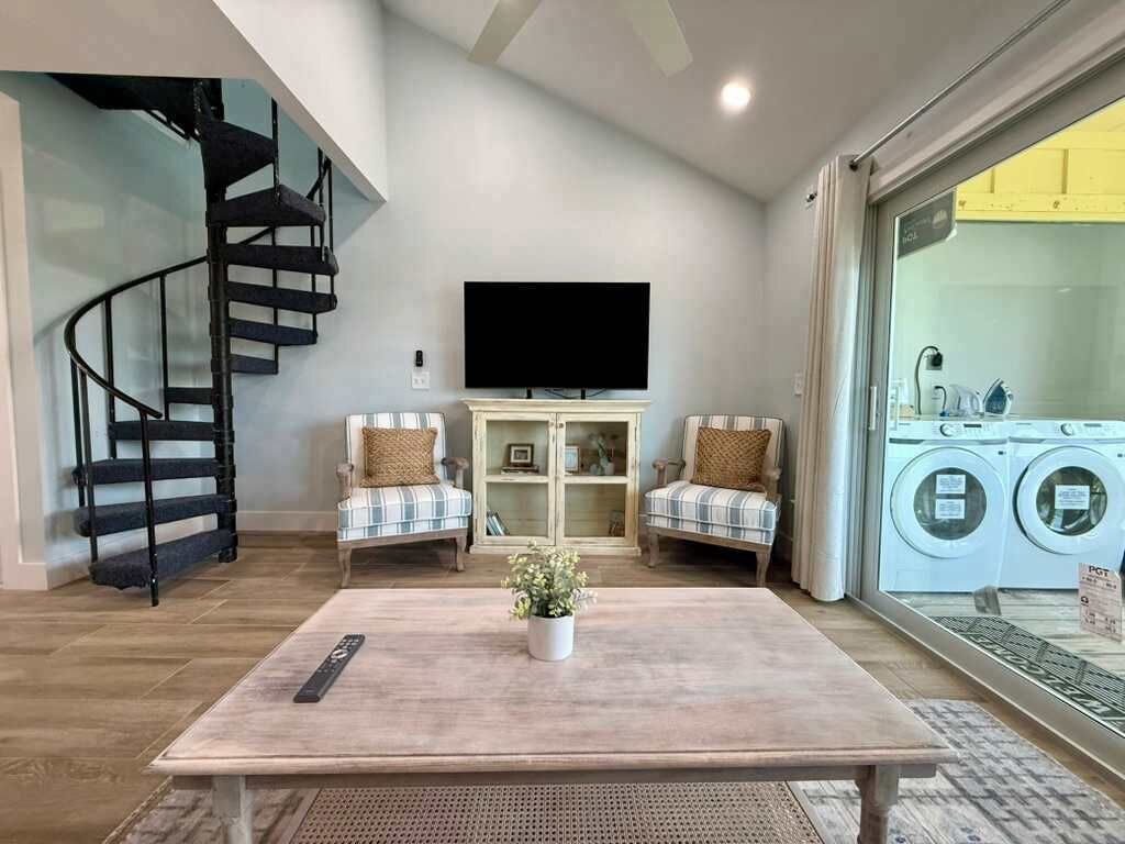 Ein Wohnzimmer mit Treppe, einem Flachbildfernseher, zwei Sesseln, einem Couchtisch und Blick auf einen Waschbereich.