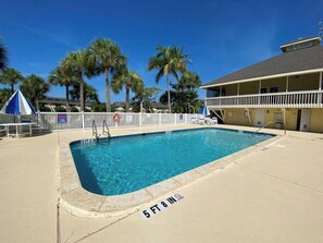 A rectangular swimming pool with a 5 ft 8 in depth marker, surrounded by a white fence, palm trees, and a building with a balcony. - Susie's LGI - Free Ferry + Golf Cart + Pool (Placida)