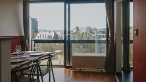 Ein Essbereich mit einem Tisch für zwei Personen, einem großen Fenster mit Vorhängen und Blick auf Gebäude.