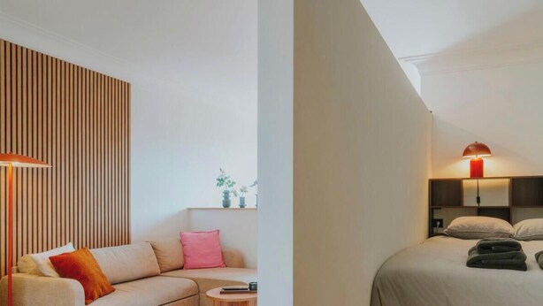 Ein modernes Hotelzimmer mit einer Couch, einem Nachttisch, einer Lampe, einem Bett mit Kissen und gefalteten Handtüchern.