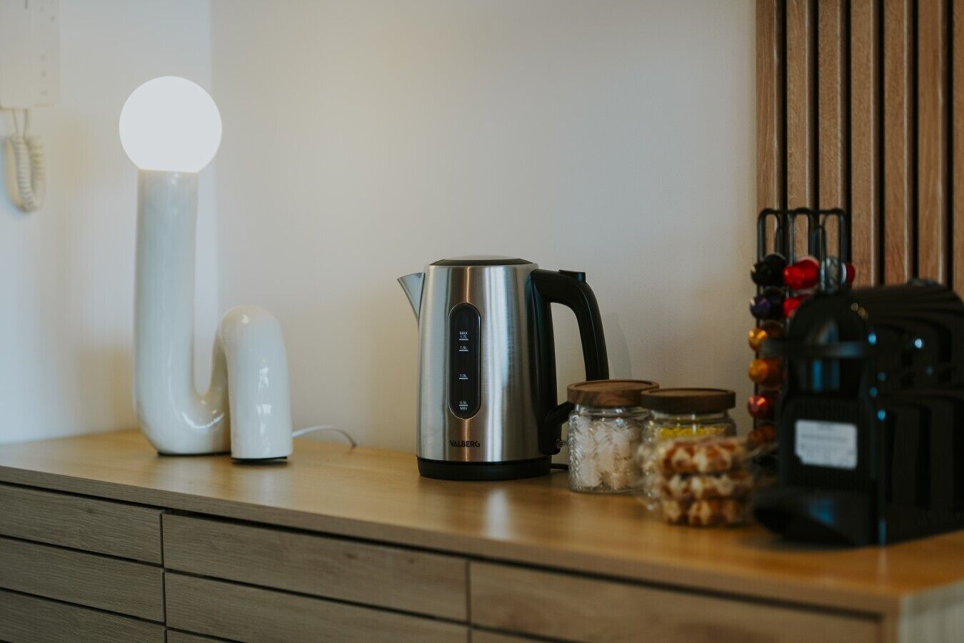 Una encimera de cocina con un hervidor de acero inoxidable, un hervidor eléctrico blanco, un tarro con tapa y un electrodoméstico negro.