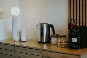 Een aanrecht met een roestvrijstalen waterkoker, een witte elektrische waterkoker, een pot met deksel, en een zwart apparaat.