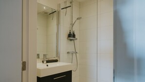 Ein modernes Badezimmer mit einem weißen Waschbecken, einem dunklen Schrank und einer Dusche inklusive Duschbrause.