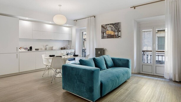Ein modernes Wohnzimmer mit einem türkisfarbenen Sofa, einem Essbereich mit weißen Stühlen und einer Küche mit weißen Schränken.