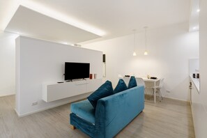A modern living room with a flat-screen TV, a blue sofa with cushions, a dining area with a table and chairs, and pendant lighting. - Moscova Boutique - One Apartment with Wi-Fi and Air Conditioning (Milan)