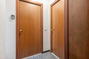 Un pasillo con dos puertas de madera, un portero automático en la pared y suelo de baldosas.