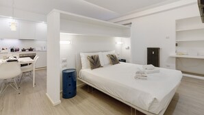 Ein modernes Hotelzimmer mit Bett, Nachttisch und Blick auf den Küchenbereich.