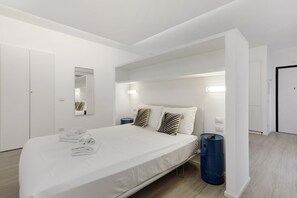 Una habitación de hotel moderna con una cama grande, una mesita de noche, un espejo y un cubo de basura azul.