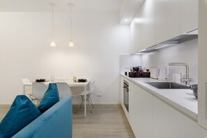 Une cuisine moderne avec des meubles blancs, un évier en acier inoxydable et un coin repas comprenant une table blanche et des chaises bleues.