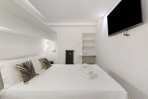 Ein modernes Hotelzimmer mit einem großen Bett, weißer Bettwäsche und einem flachbildfernseher an der Wand.