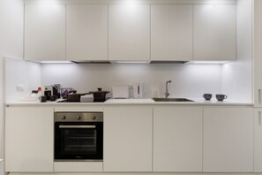 Eine moderne Küche mit weißen Schränken, einem Einbauofen, einer Spüle und verschiedenen Geräten.
