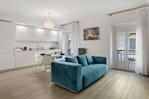 A modern living room with a teal sofa, a dining area with a white table and chairs, and a kitchen with white cabinets and appliances. - Moscova Boutique - Two Apartment with Wi-Fi and Air Conditioning (Milan)