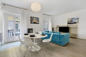 A modern living room with a blue sofa, a dining table with chairs, and a flat-screen TV mounted on the wall. - Moscova Boutique - Two Apartment with Wi-Fi and Air Conditioning (Milan)