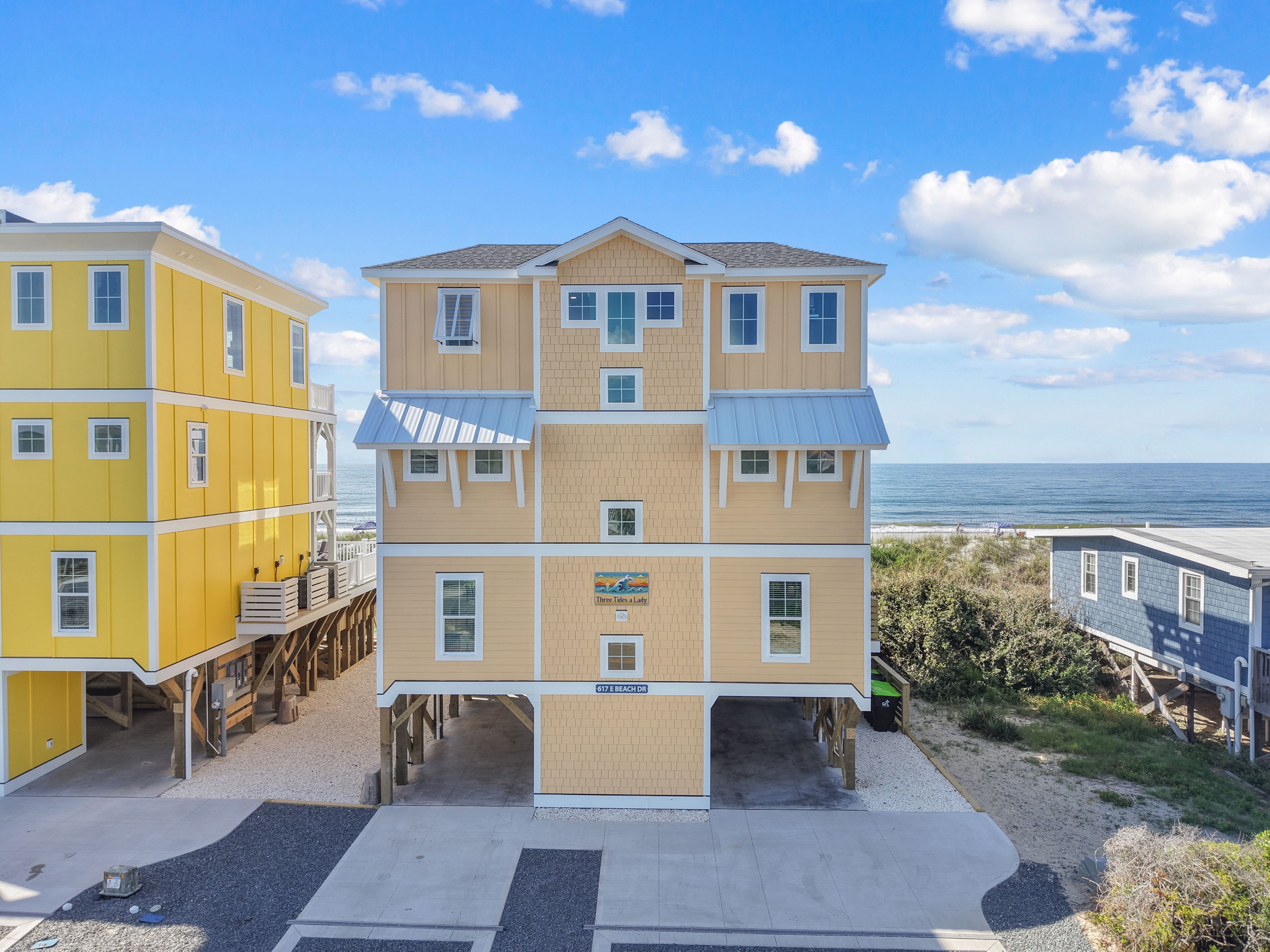 A multi-story building with a beach view, featuring a balcony on the first floor and a sign indicating the address.