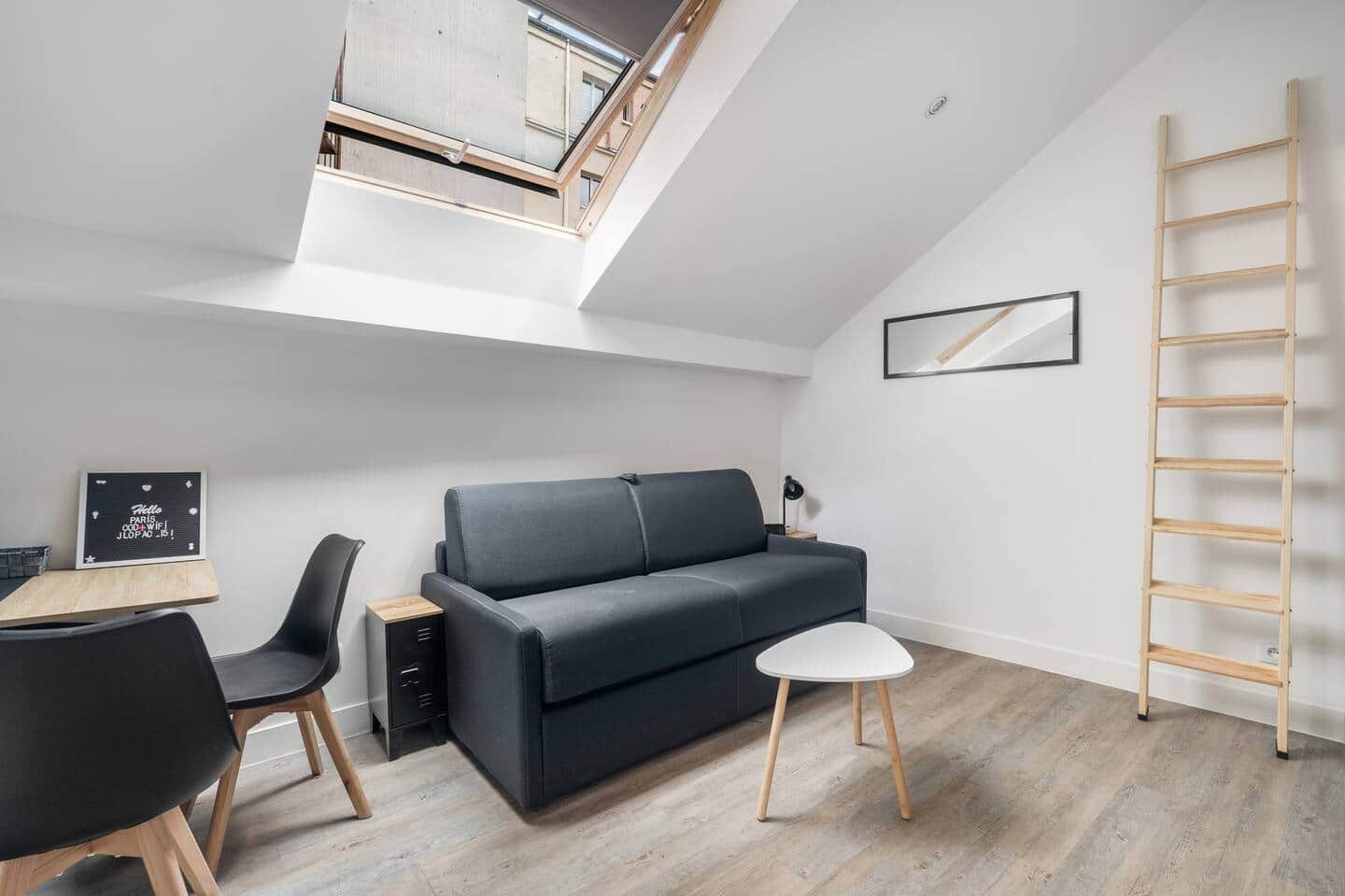 A compact living space with a loft bedroom, a sofa, a dining table, and a ladder.