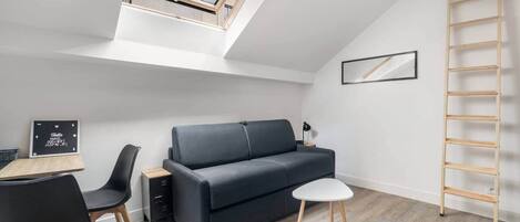 A compact living space with a loft bedroom, a sofa, a dining table, and a ladder.