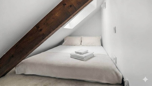 A small, white, sloped ceiling room with a bed, pillows, and a neatly folded blanket. - Cozy Studio - Eiffel Tower (Paris)
