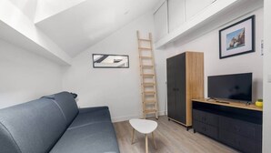 A compact living space with a gray sofa, a white chair, a wooden ladder, a TV on a wooden stand, and a cabinet. - Cozy Studio - Eiffel Tower (Paris)