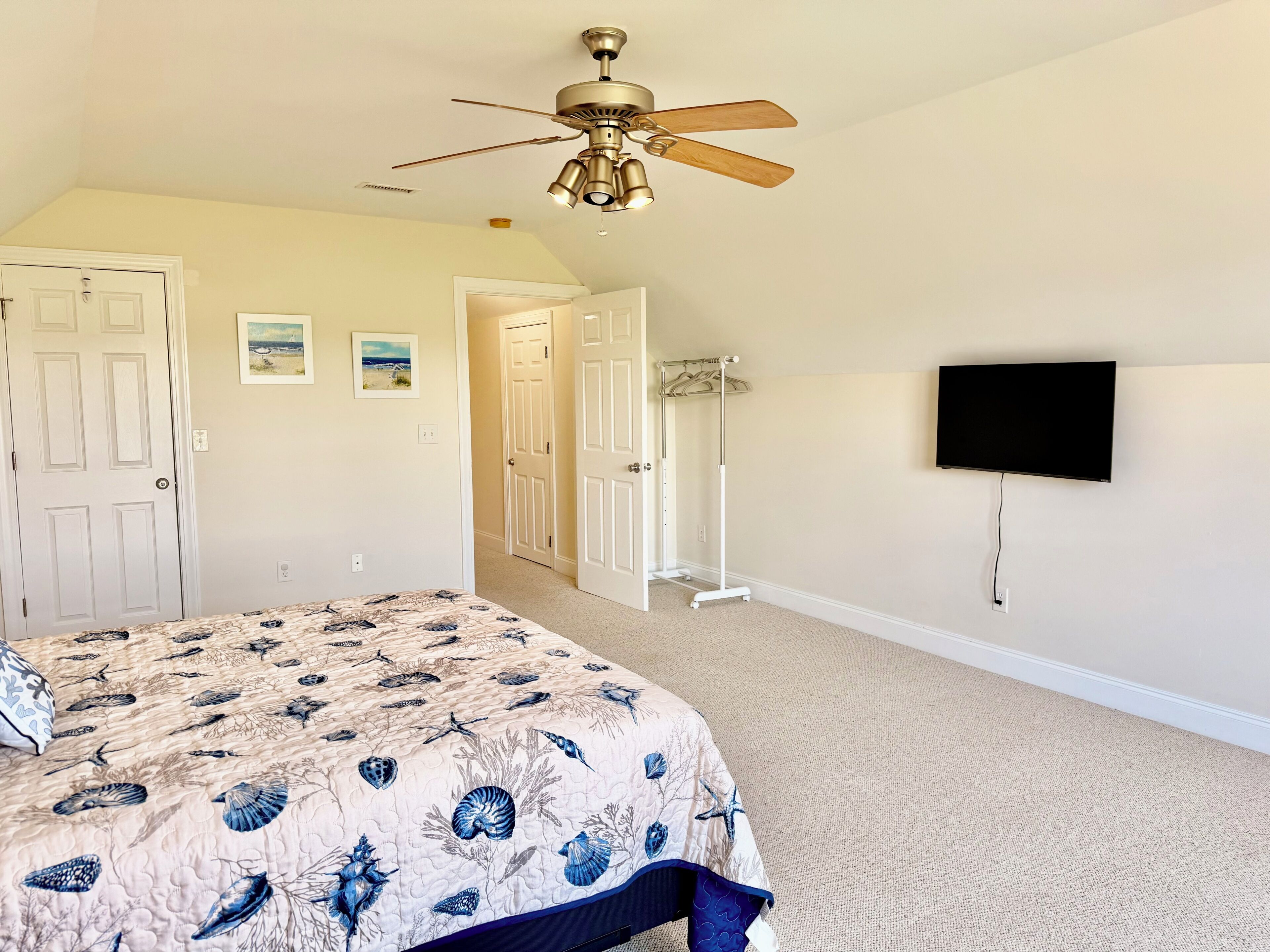 A bedroom with a bed, a ceiling fan, a television, and a hallway leading to another room.